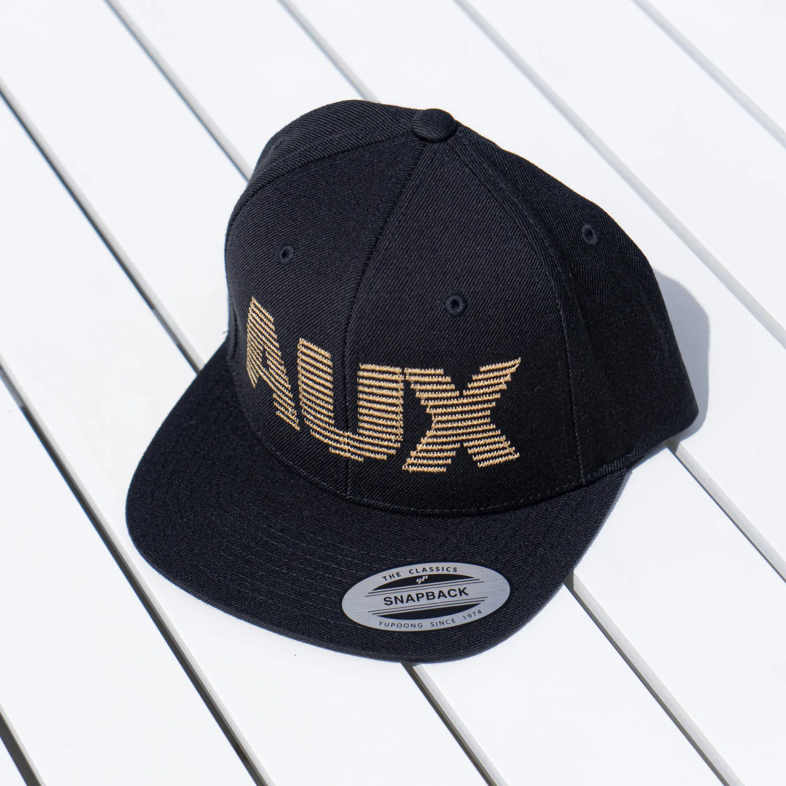 AUX Mono Gold Snapback Cap auf weißem Holz
